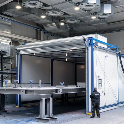 Greis-Mitarbeiter vor innovativer Teleskop-Trocknungsanlage zur Beschleunigung von Beschichtungsprozessen