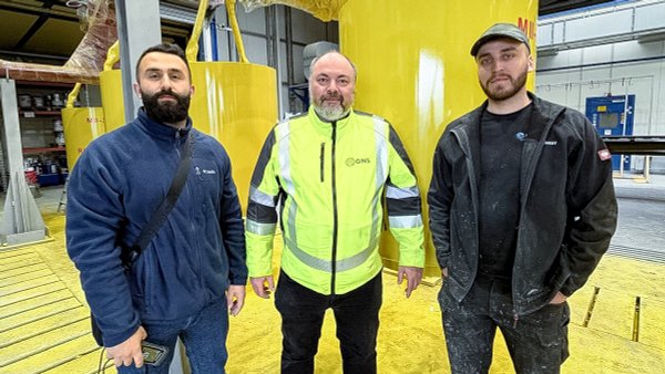 Teammitglieder von GREIS und GNS vor beschichteten gelben Hochdruckkomponenten.